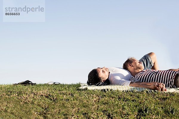 Erwachsenes männliches Paar auf Picknickdecke im Park liegend