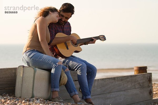 Junges Paar am Strand  Mann spielt Gitarre