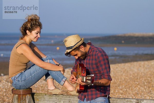 Junges Paar am Strand  Mann spielt Gitarre
