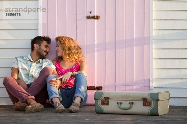 Junges Paar sitzend bei Strandhütte mit Koffer