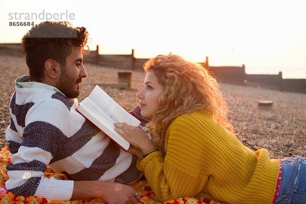 Junges Paar am Strand liegend  Frau liest Buch