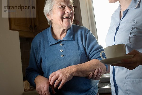 Körperpflege-Assistentin mit einer Tasse Tee für Seniorinnen