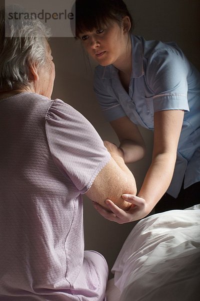 Körperpflege-Assistentin hilft Seniorin aufzustehen