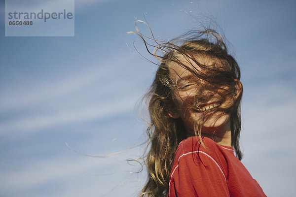 Ein lächelndes neunjähriges Mädchen  dem der Wind die Haare übers Gesicht weht.