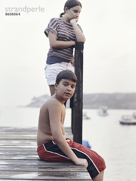 Zwei junge Leute  Teenager  Junge und Mädchen  auf einem Dock mit Blick auf vertäute Boote an der Küste.