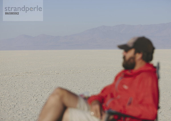 Mann sitzt auf einem Stuhl in der weiten  kargen Wüste  verschwommener Fokus