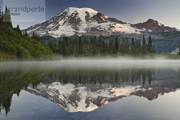 Mount Rainier  ein schneebedeckter Gipfel  umgeben von Wald  der sich in einem der vielen Seen des Mount Rainier Nationalparks spiegelt.