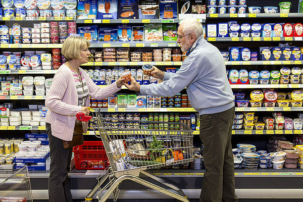 Seniorenpaar mit Einkaufswagen beim Einkaufen im Supermarkt  Kühlregal mit Molkereiprodukten  Deutschland