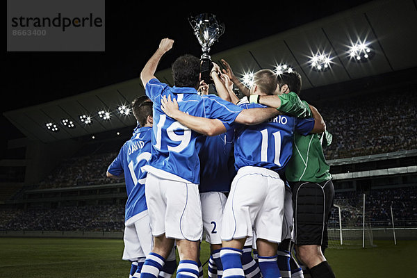 Fußballmannschaft jubelt mit Trophäe auf dem Spielfeld