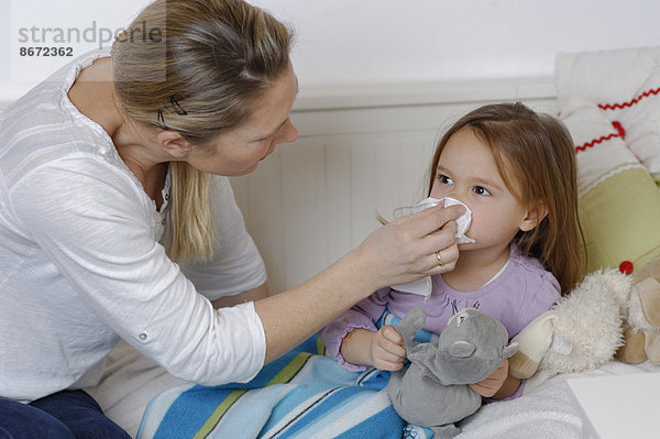 Mutter kümmert sich um ihre kranke Tochter  putzt die Nase  Mädchen liegt im Bett