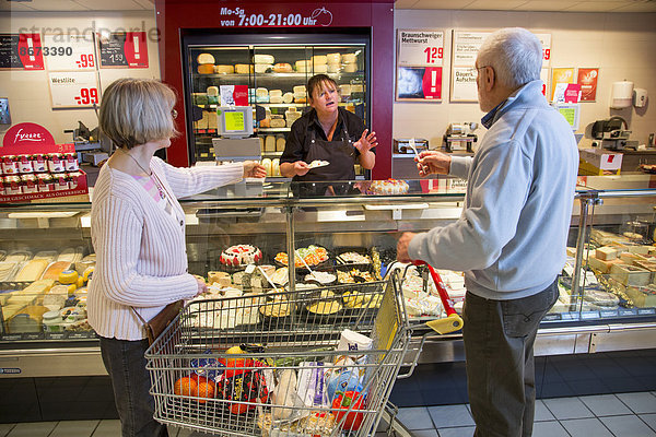 Seniorenpaar mit Einkaufswagen beim Einkaufen im Supermarkt  an der Käsetheke  Deutschland