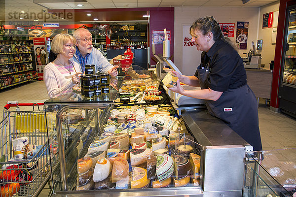 Verkäuferin bedient ein Seniorenpaar an der Käsetheke  beim Einkaufen im Supermarkt  Deutschland