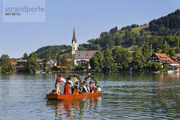 Trachtler in einer festlich geschmückten Plätte  Holzboot  hinten die Kirche St. Sixtus  Alt-Schlierseer-Kirchtag  Schliersee  Oberbayern  Bayern  Deutschland