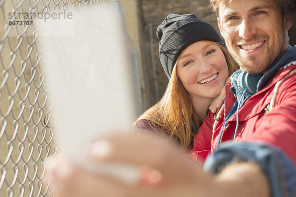 Selbstporträt eines Paares mit Fotohandy neben dem Kettengliederzaun