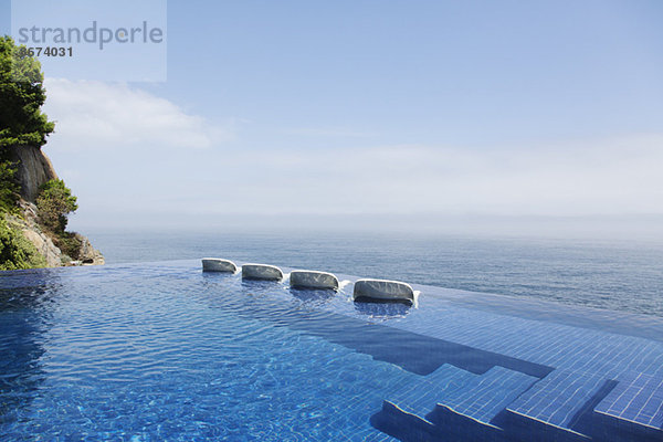 Liegestühle im Infinity-Pool mit Blick auf den Ozean