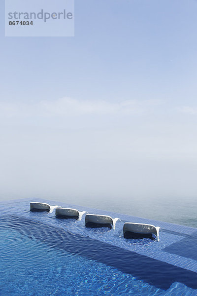 Liegestühle im Infinity-Pool mit Blick auf den Ozean