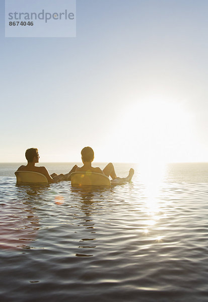 Paar in Liegestühlen im Infinity-Pool mit Blick auf den Ozean