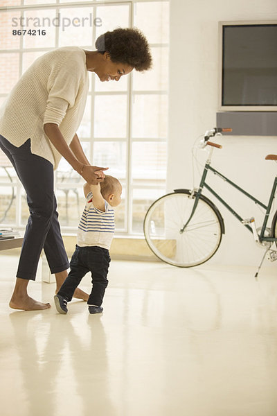 Mutter hilft dem kleinen Jungen im Wohnzimmer zu laufen