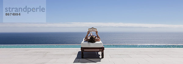 Frau entspannt sich auf einem Liegestuhl am Pool mit Blick aufs Meer