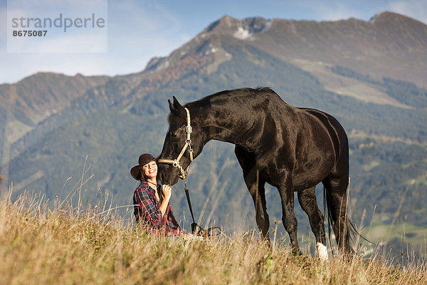 Junge Frau mit Hannoveraner  Rappe  auf Bergwiese im Herbst  Nordtirol  Österreich