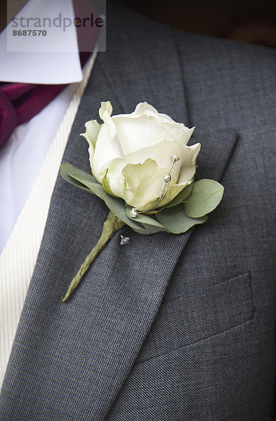 Ein Bräutigam in grauer Jacke und weißem Hemd  mit einer weißen Rosenboutonniere im Knopfloch.