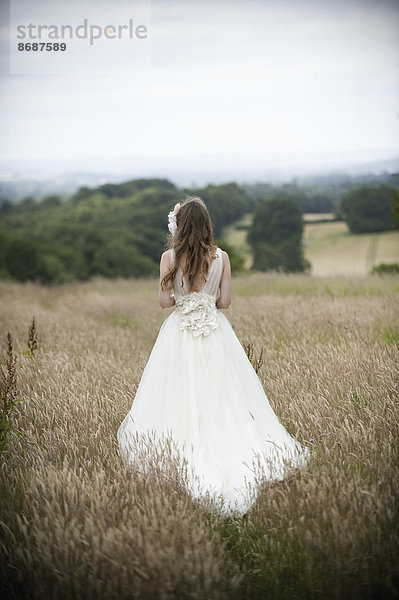 Eine Braut in ihrem Brautkleid  die auf einem Feld steht.