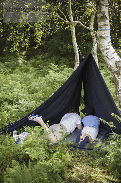 Zwei Jungen zelten im New Forest und liegen unter einem Zeltschutzdach.