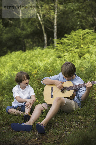 Zwei Jungen zelten in New Forest. Sitzen auf dem Gras  einer spielt Gitarre.