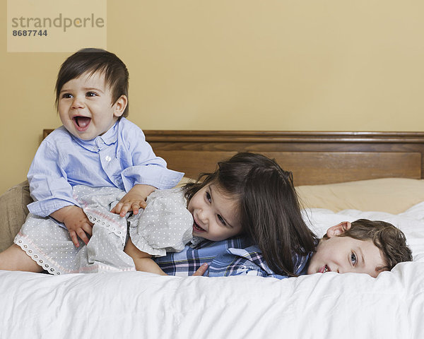 Drei Kinder einer Familie  die spielend auf einem großen Bett liegen.