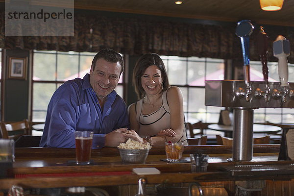 Ein Mann und eine Frau sitzen lächelnd nebeneinander an einer Bar. Bei einer Verabredung.