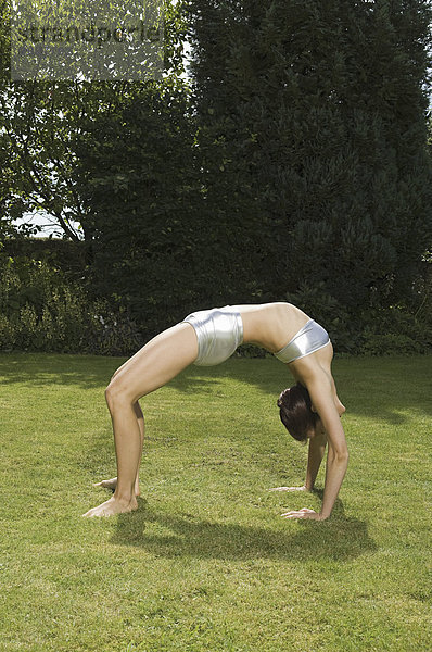 Eine junge Frau zeigt ihre Beweglichkeit  lehnt sich in einem Bogen nach hinten  Hände und Füße auf Gras