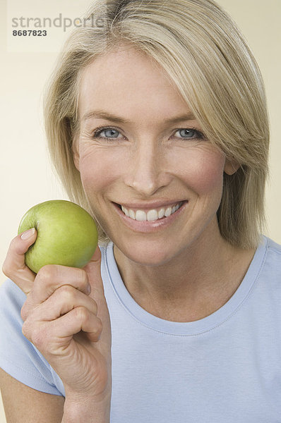 Eine junge Frau hält einen grünen Apfel.