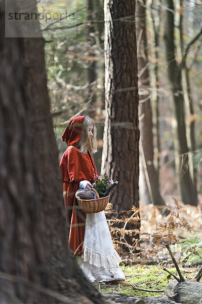 Mädchenmaskerade als Rotkäppchen im Wald stehend