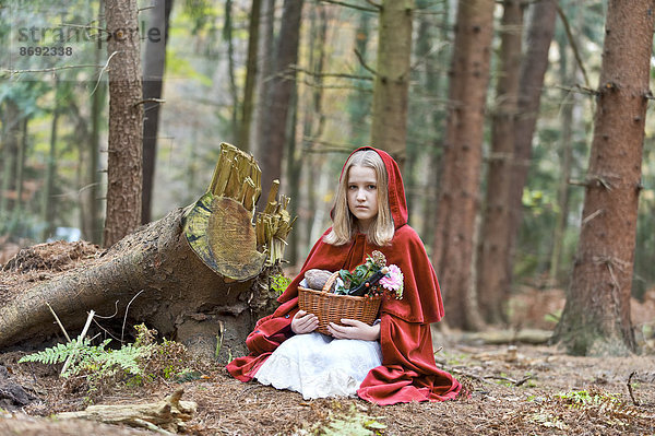 Mädchenmaskerade als Rotkäppchen auf dem Boden im Wald sitzend