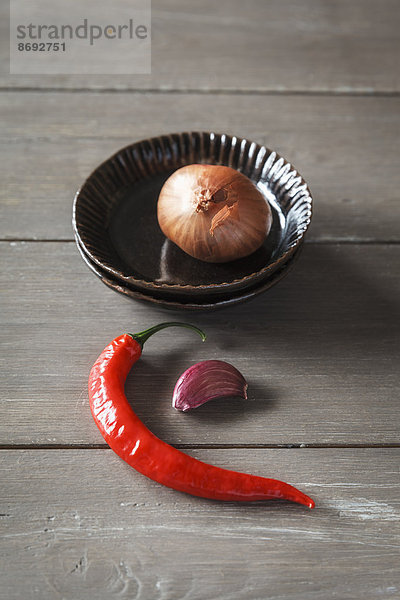 Rote Chilischote  Knoblauchzehe und Zwiebel auf Holztisch