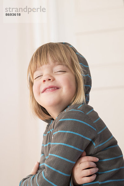 Porträt eines lächelnden kleinen Mädchens mit geschlossenen Augen und Kapuzenpullover