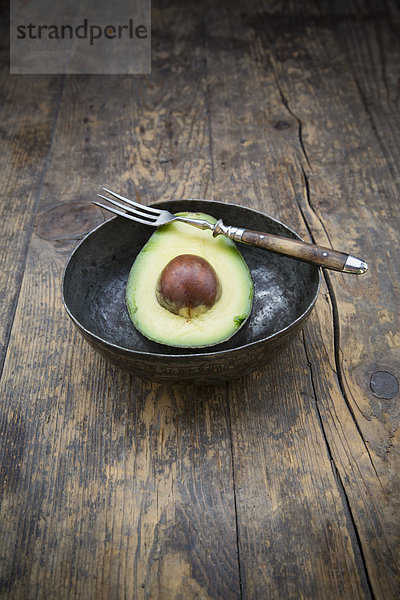 Schale mit halber Avocado (Persea Americana) auf Holztisch