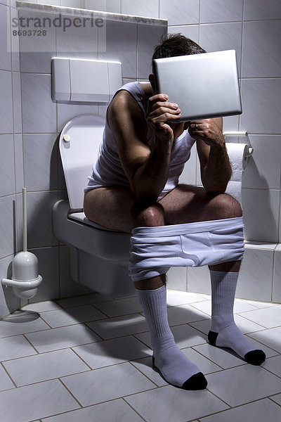 Deutschland  Mann auf Toilette sitzend  mit digitalem Tablett