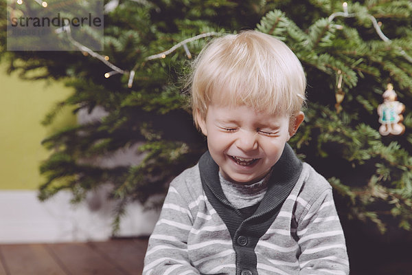 Lachendes Kleinkind unter dem Weihnachtsbaum zu Hause