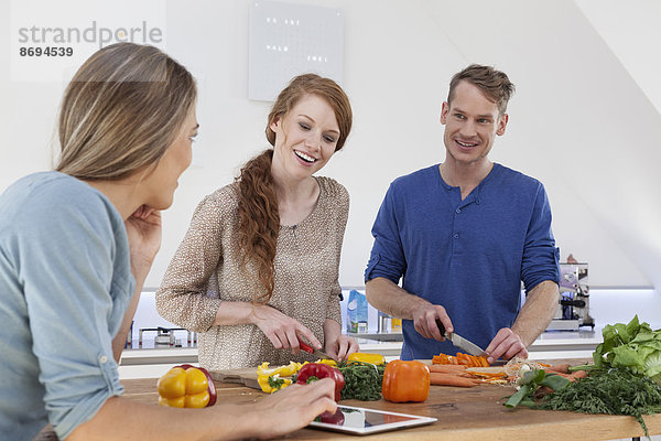 Drei Freunde beim Zubereiten des Essens und mit dem Tablet-Computer
