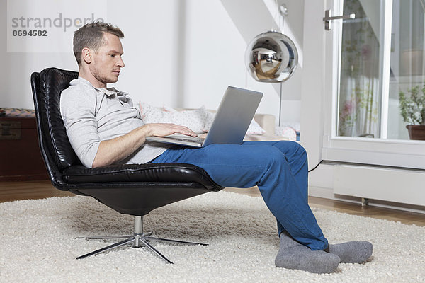 Mann zu Hause entspannt im Sessel mit Laptop