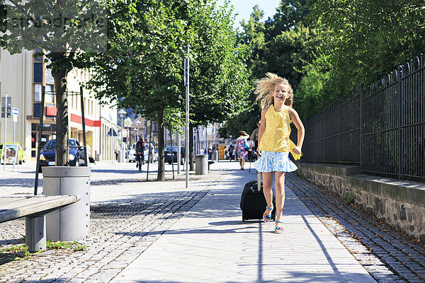 Mädchen mit auf dem Bürgersteig laufendem Zugkoffer