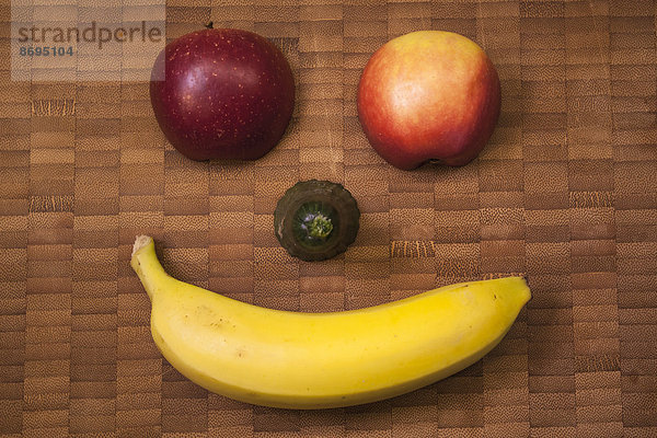 Lustiges Fruchtgesicht mit Banane  Gurke und Apfel auf Holztisch  Nahaufnahme