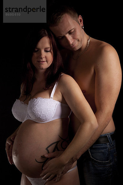 Mann umarmt schwangere Frau von hinten