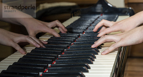 Zwei Hände spielen Klavier und spiegeln sich dabei im Instrument