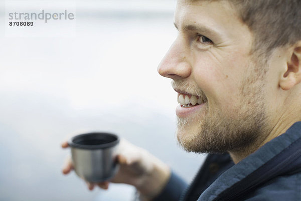 Glücklicher Mann hält Kaffeetasse gegen den See