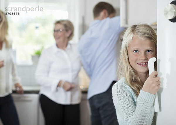 Porträt des lächelnden Mädchens mit Türgriff und Familie im Hintergrund in der Küche