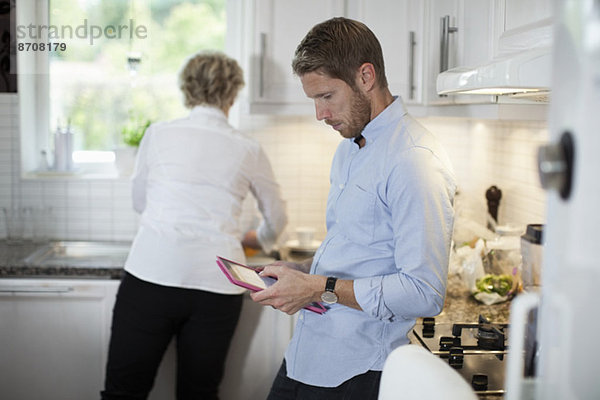 Mann mit digitalem Tablett und Mutterkochen in der Küche