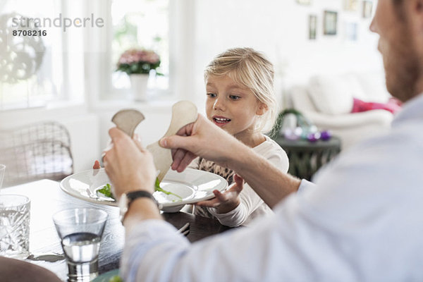 Vater serviert Salat an Tochter am Esstisch