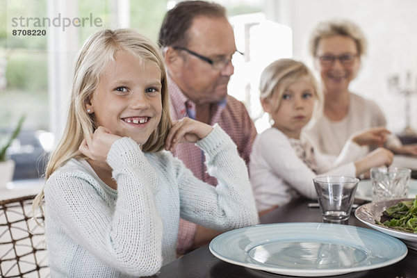 Porträt eines glücklichen Mädchens  das mit seiner Familie am Esstisch sitzt.